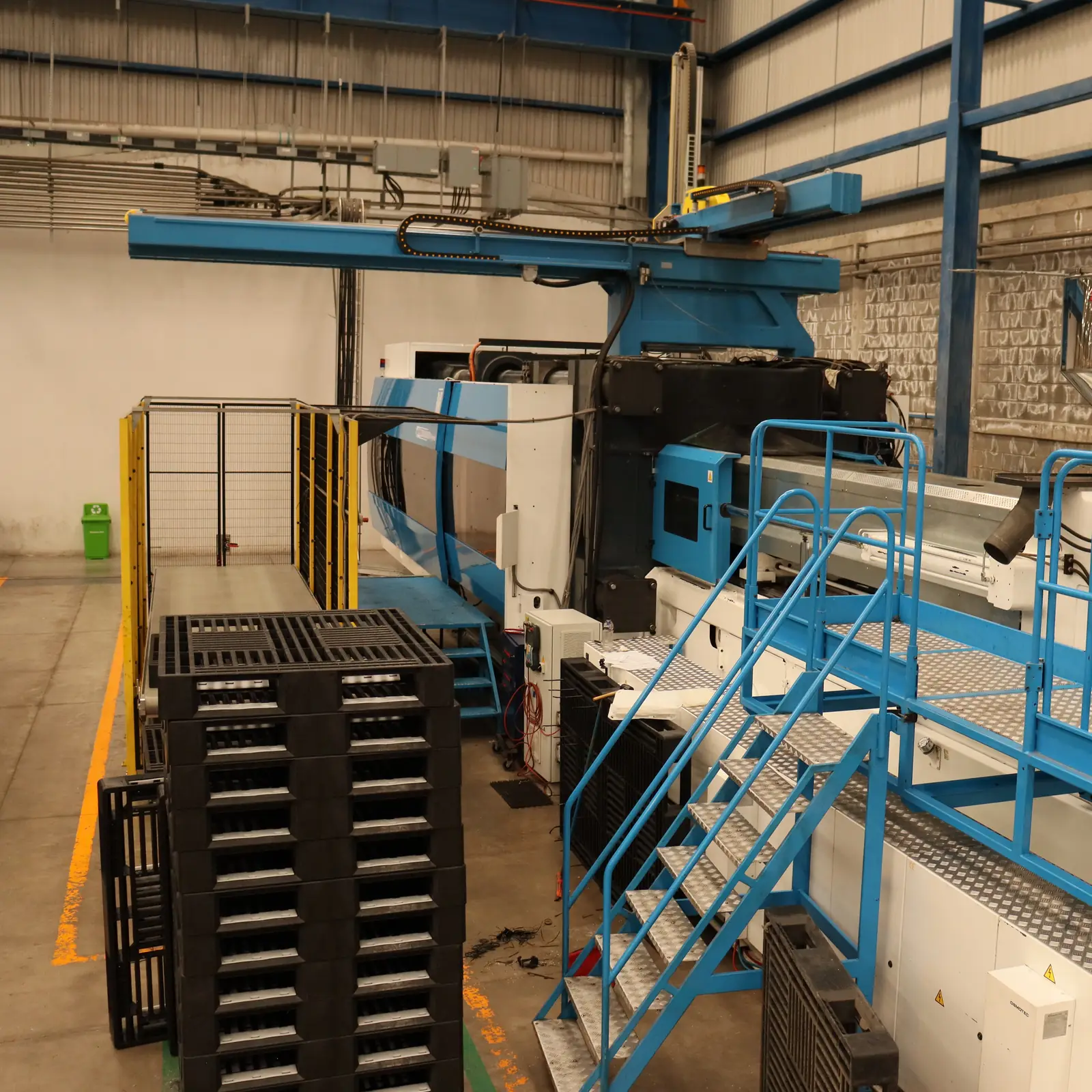 Máquina de inyección de la planta de Europlast junto a una estiba de tarimas de plástico negras